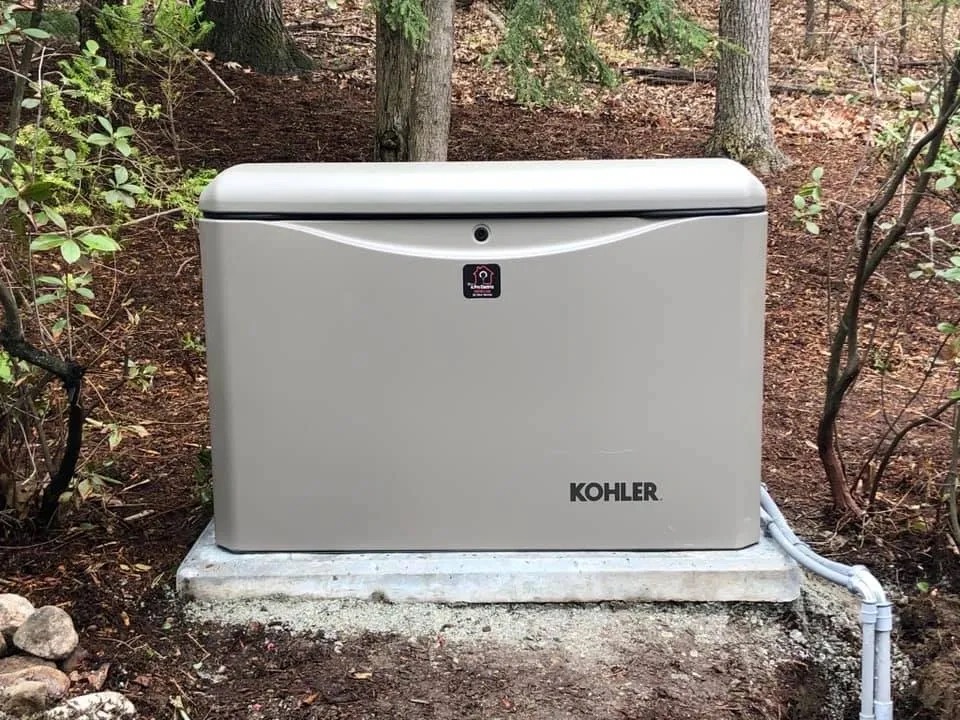 Kohler standby generator installed on a pad beside a wooded lot